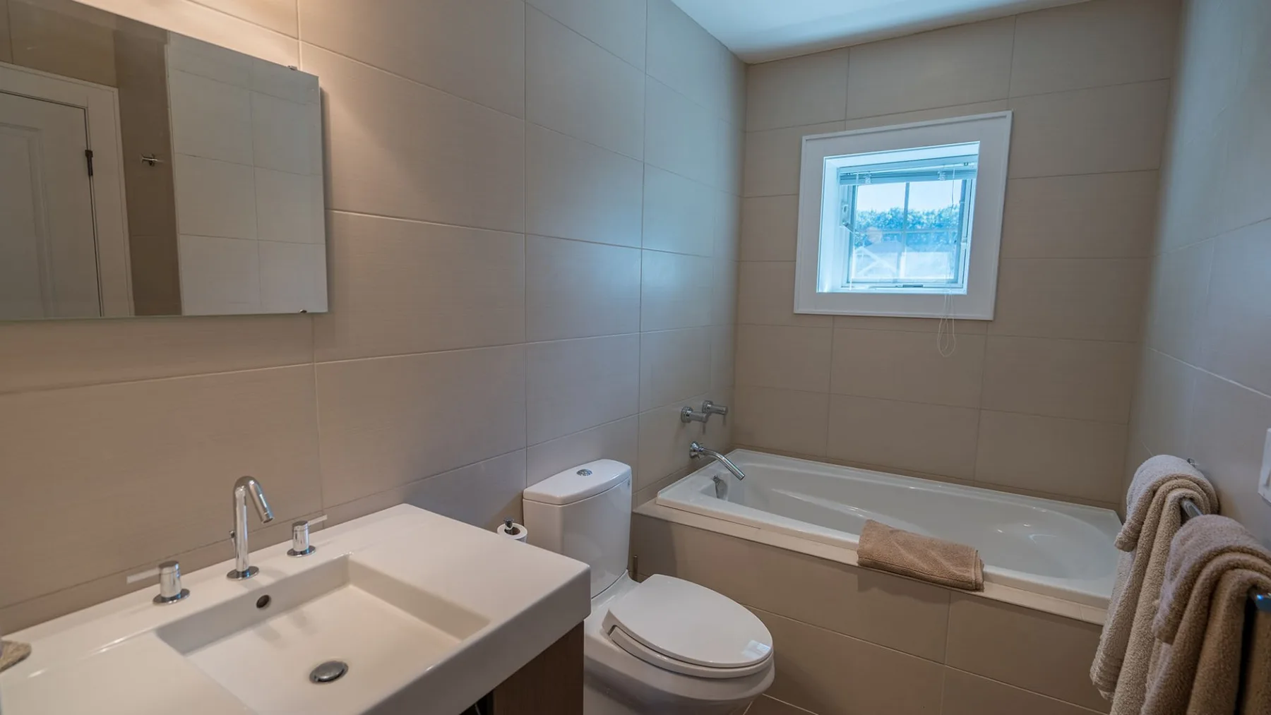 A tiled bathroom with a sink, toilet, and bathtub beneath a window.