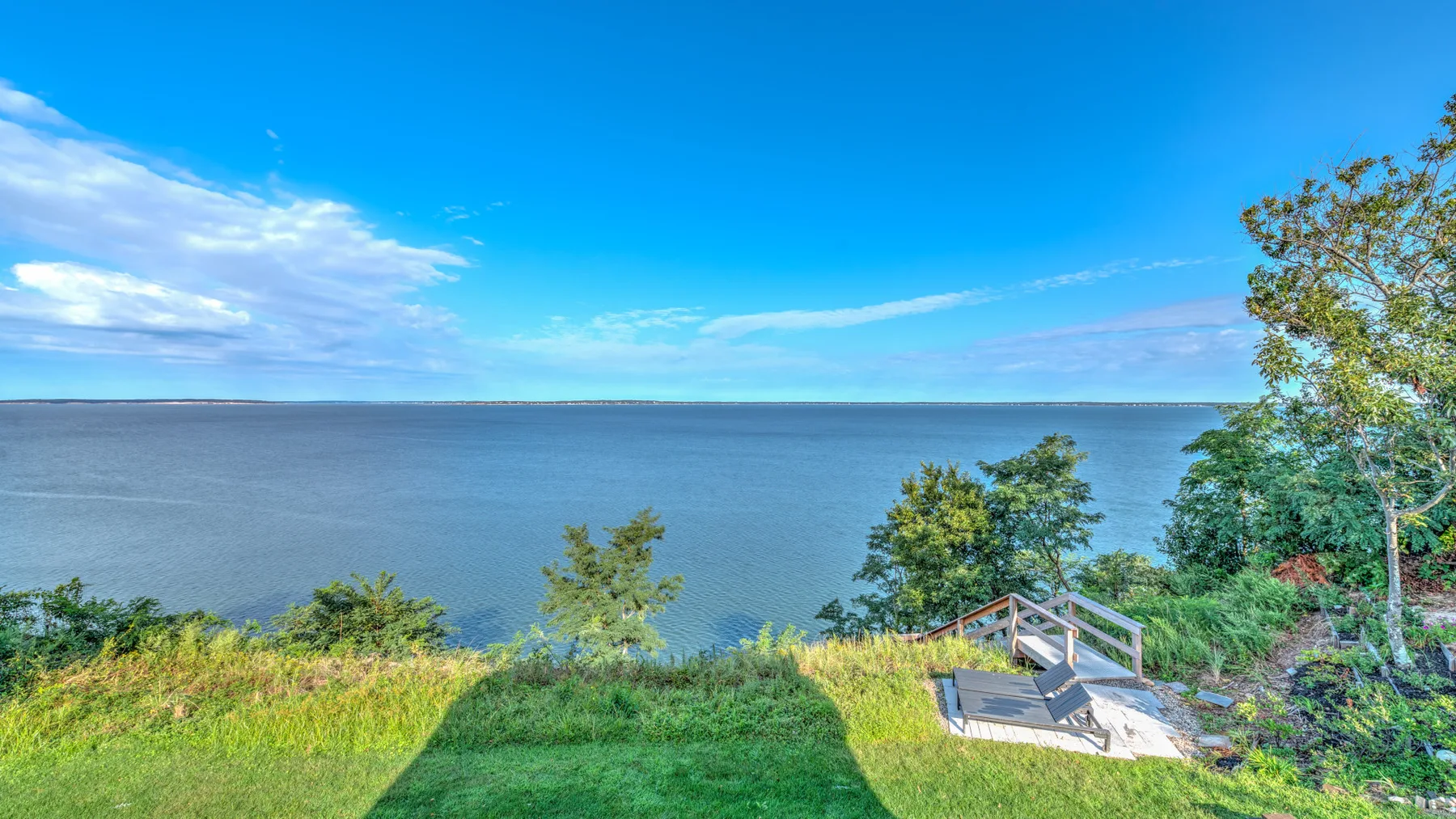 A grassy waterfront overlooks calm water, with a small wooden viewing platform nearby.