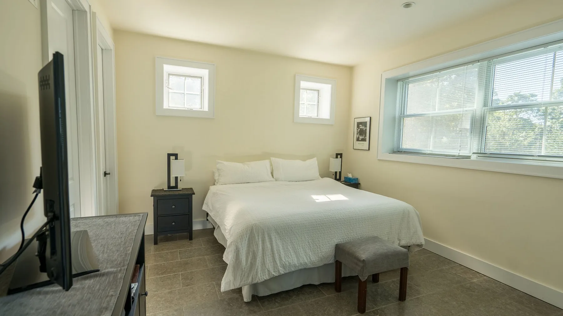 A bright bedroom with a neatly made bed and a large window.