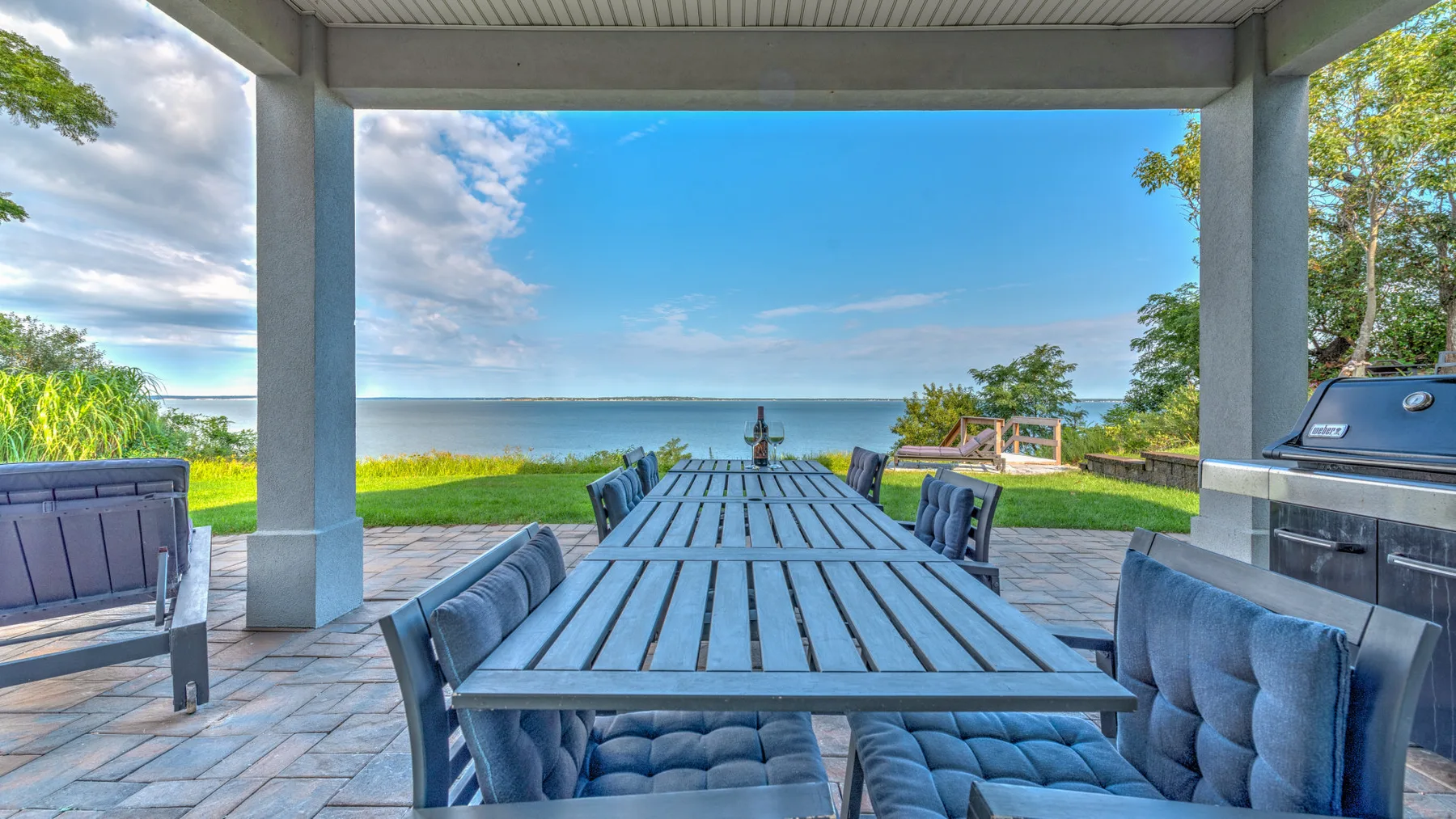 A covered outdoor dining area overlooks a lawn and the water.