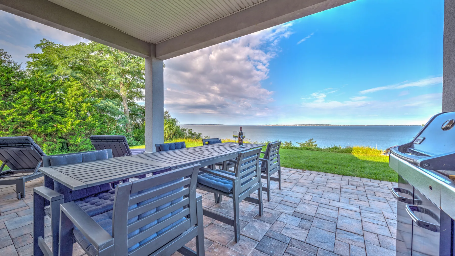 A covered outdoor dining area overlooks a lawn and the water.