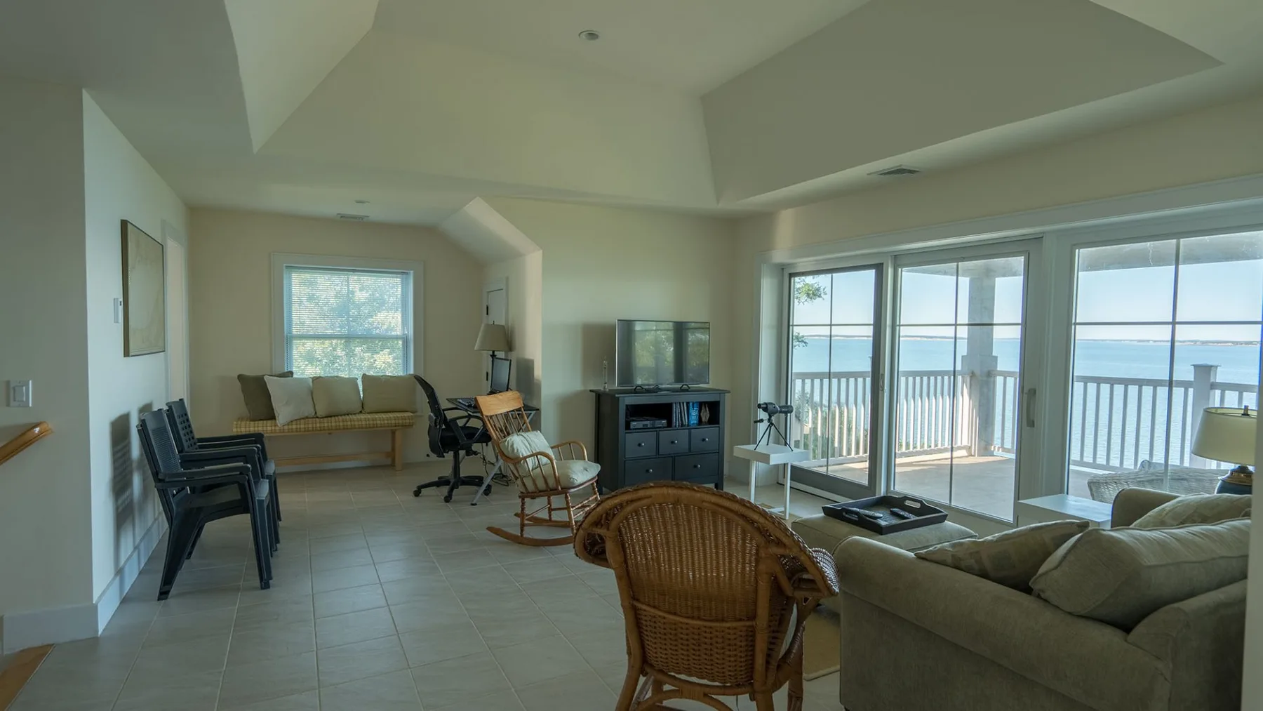A bright living room with seating arranged beside large windows overlooking the water.