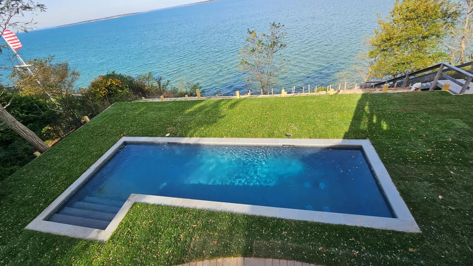 A rectangular swimming pool sits in a grassy yard overlooking the water.