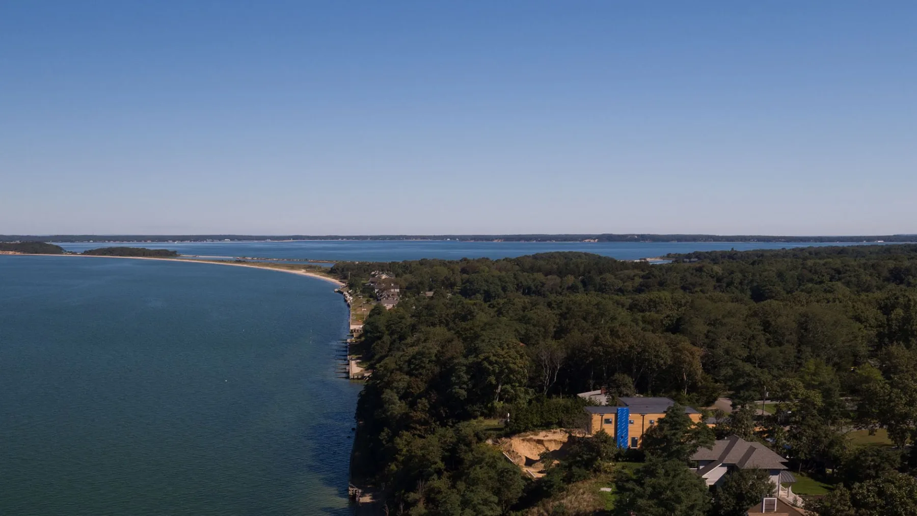 Aerial view of a wooded shoreline beside a broad body of water.