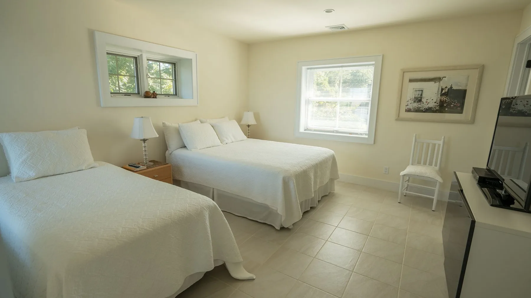 A bright bedroom with two beds, windows, and a small television.