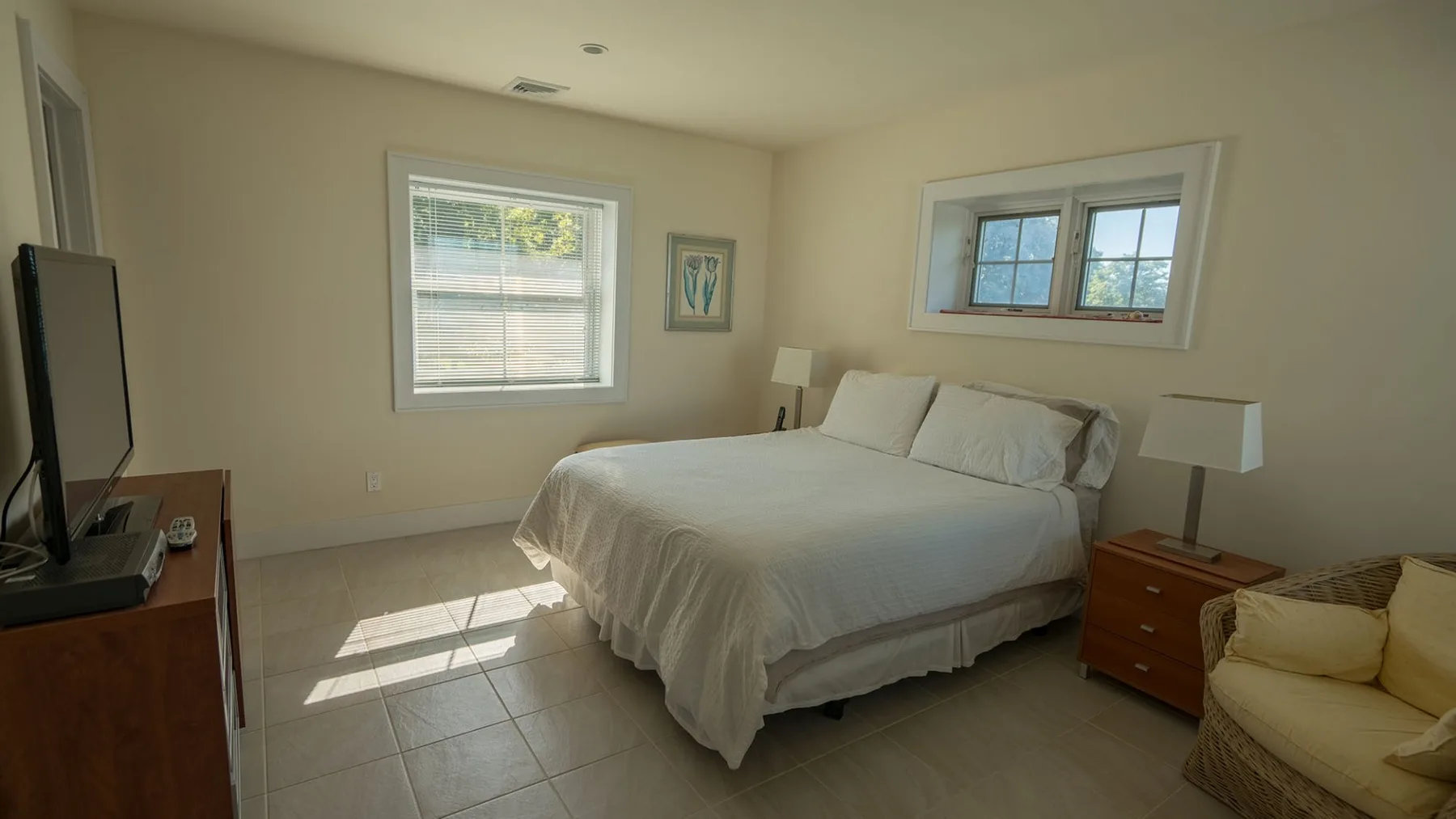 A bedroom with a neatly made bed and windows letting in daylight.