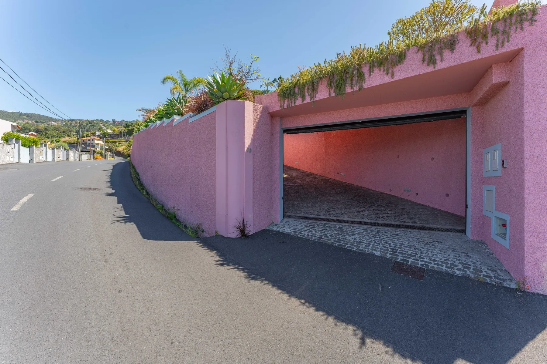 A pink walled driveway entrance opens onto a sloped paved garage area.