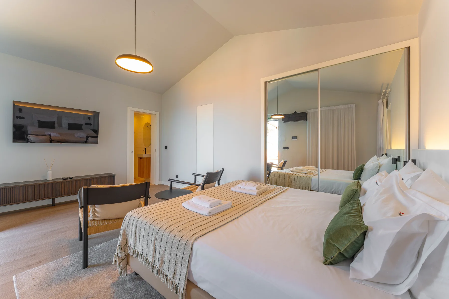 A bedroom with a neatly made bed and a large wall mirror.