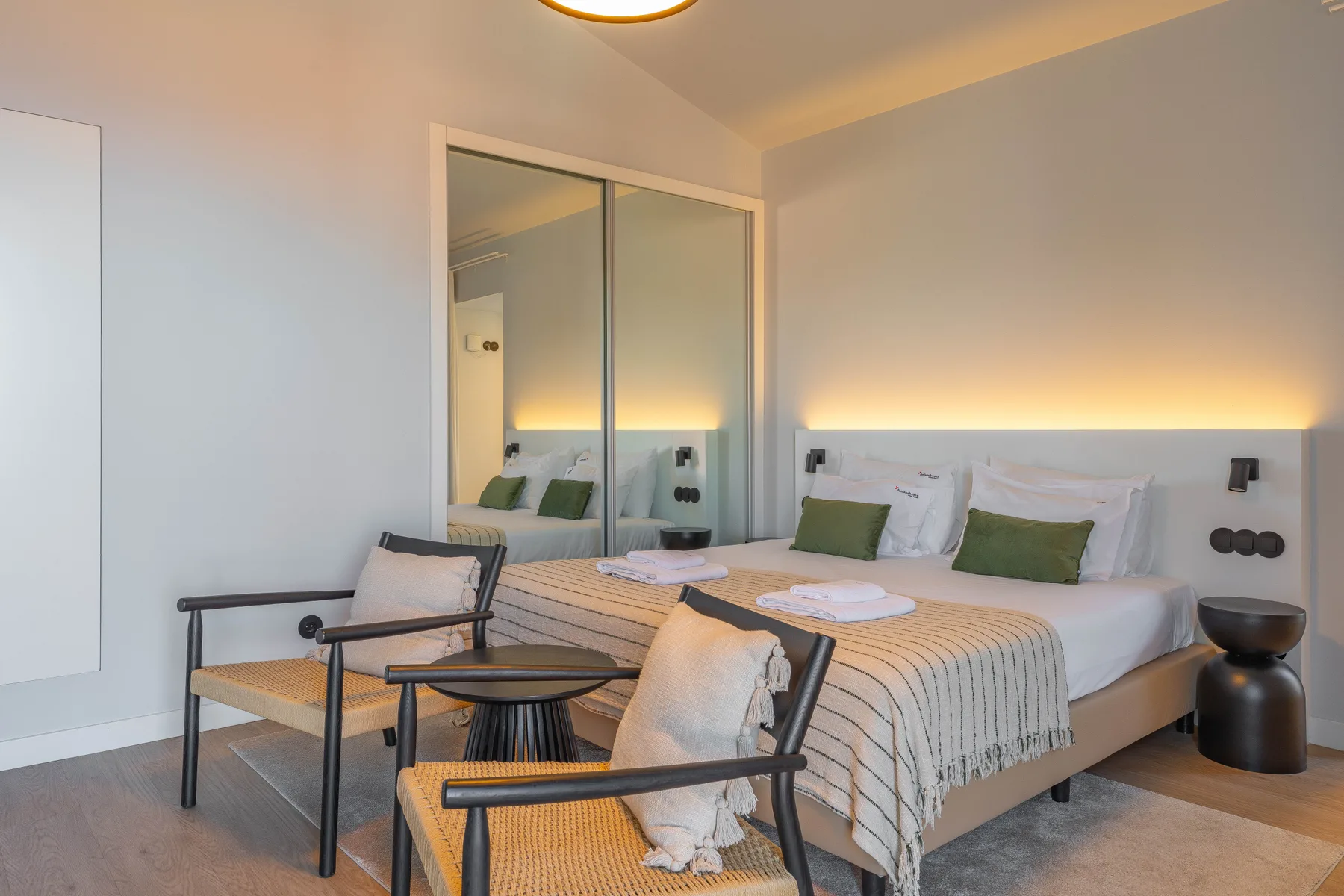 A bedroom with a neatly made bed and two chairs beside a small table.