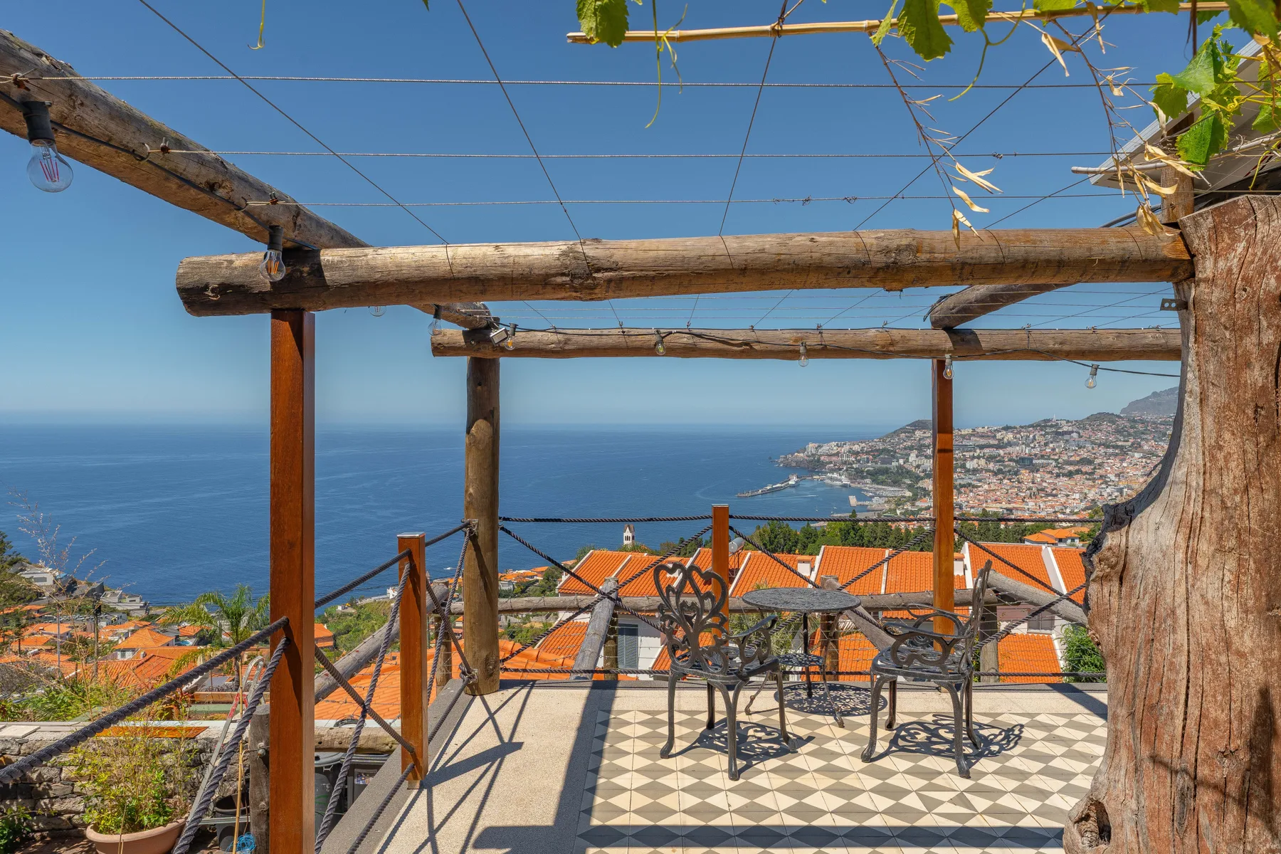 A terrace with outdoor seating overlooks the sea and coastal hillside.