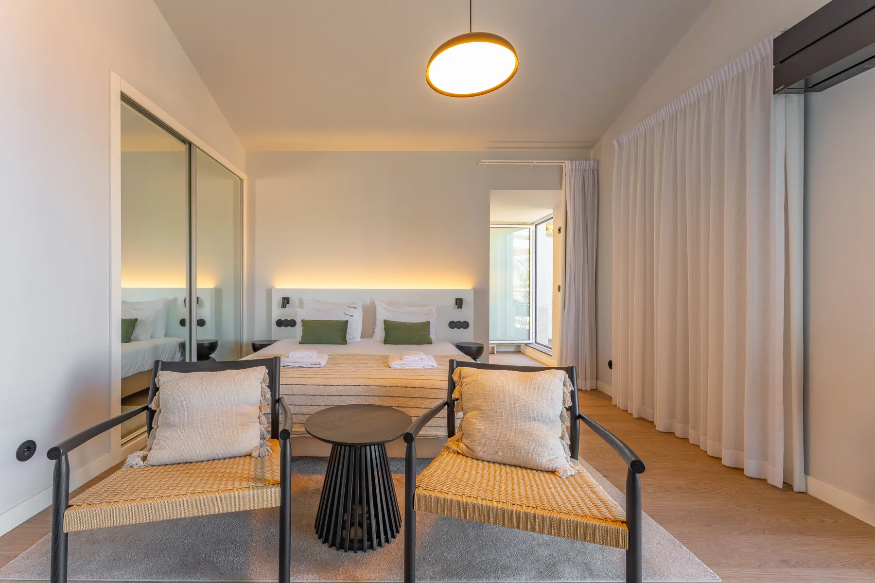 A bedroom with a bed, two armchairs, and floor-to-ceiling curtains.