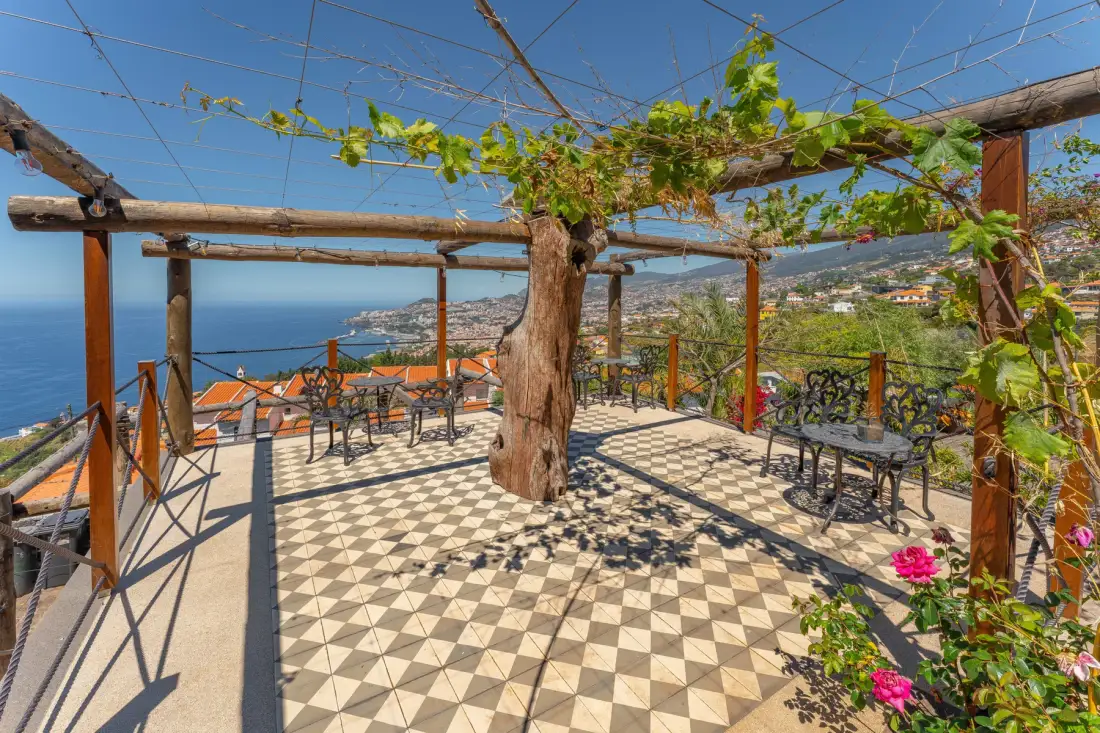 A tiled outdoor terrace with vine-covered beams overlooks the sea and hillside.