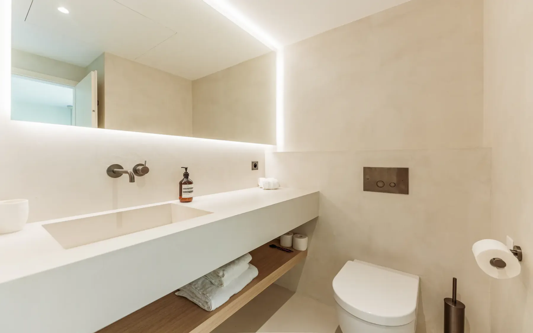 Baño blanco moderno con un lavabo blanco, un espejo grande retroiluminado y un inodoro a la derecha.