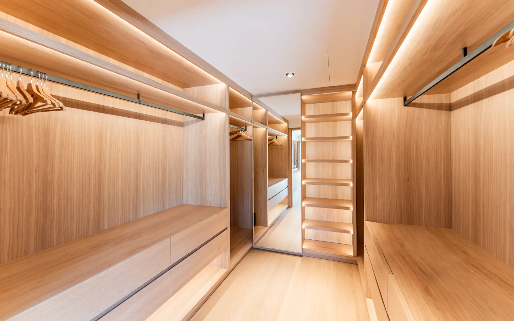 Amplio vestidor de madera con barras para colgar ropa, estantes y un espejo alto.