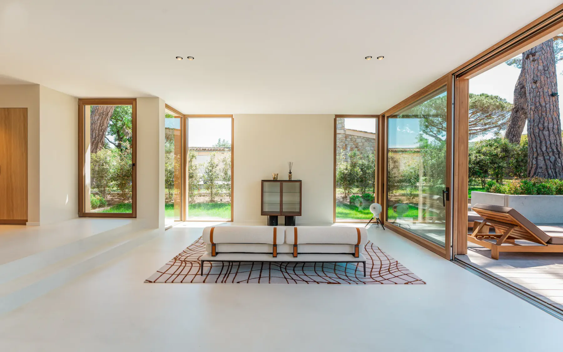 Sala de estar luminosa con un sofá blanco y grandes ventanales con vistas a los árboles.
