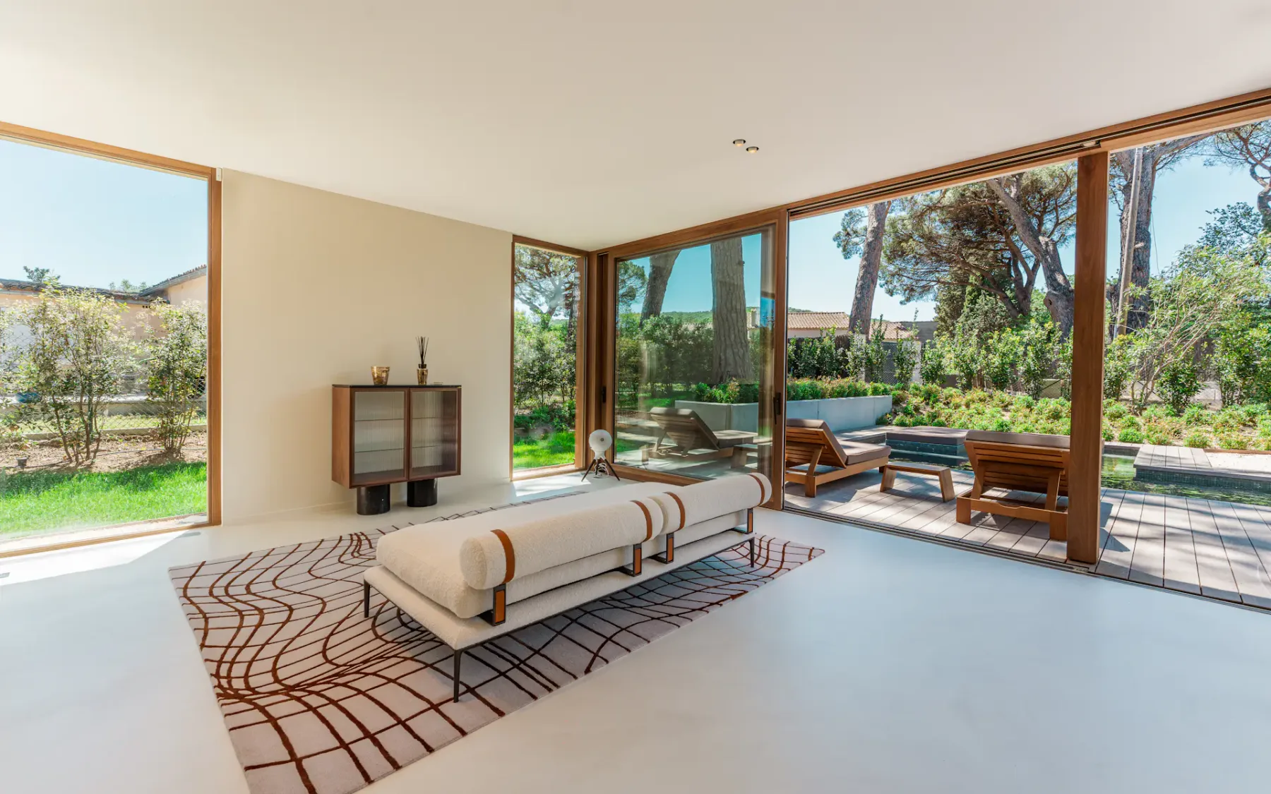 Una sala luminosa con asientos bajos junto a grandes ventanales que dan a un jardín.