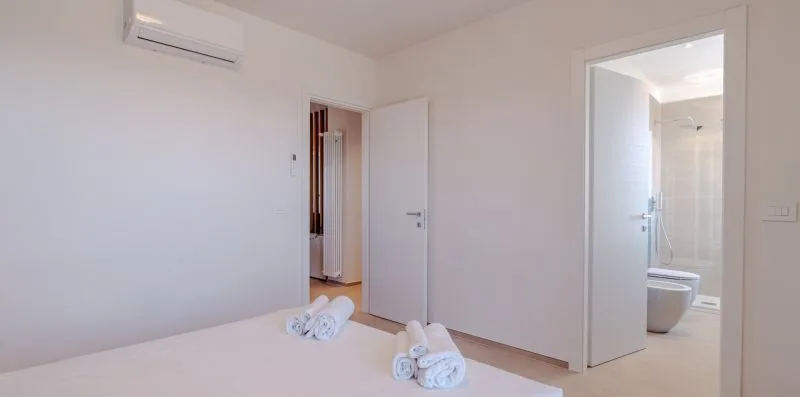 Un dormitorio luminoso con ropa de cama blanca y una puerta abierta al baño.