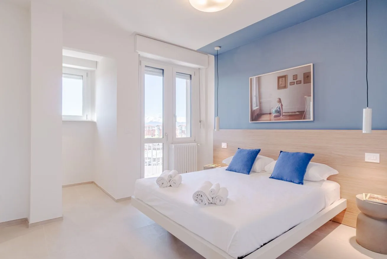 Un dormitorio luminoso con una cama blanca y una pared azul.