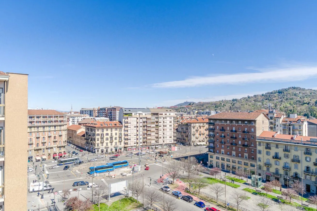 Una plaza urbana rodeada de edificios y calles, con colinas a lo lejos y cielo despejado.