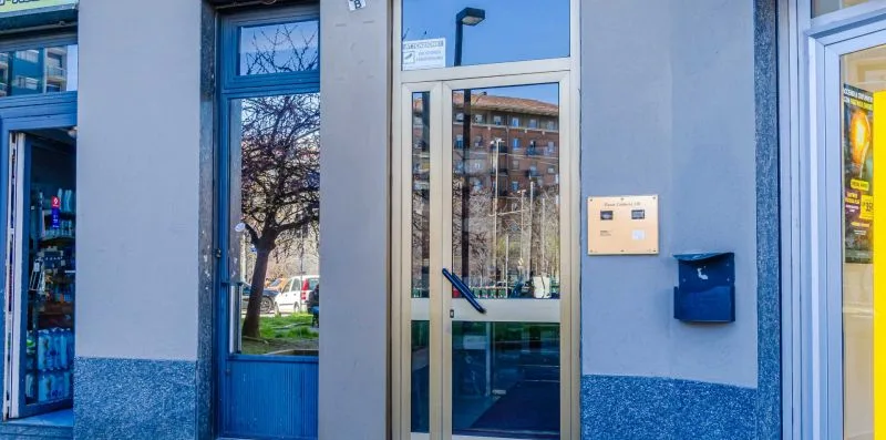 Entrada de un edificio con puerta de vidrio, ventanas y un buzón en la pared.