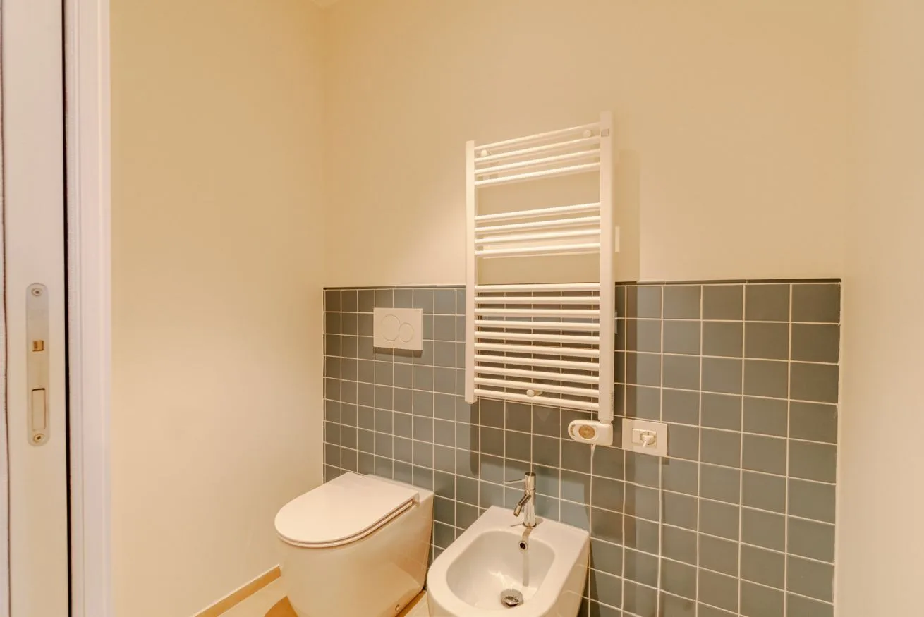 Un baño con inodoro, bidé y radiador toallero de pared.