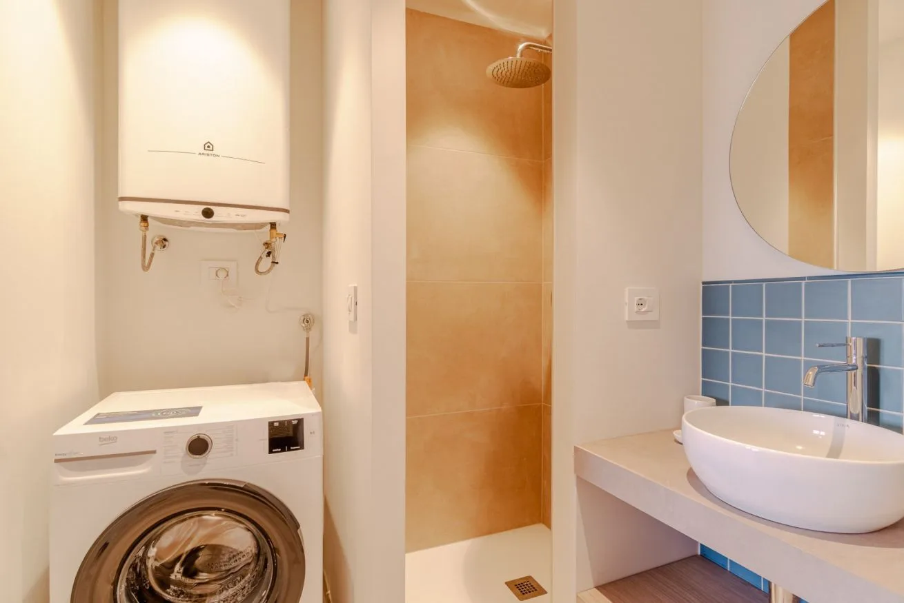 Un baño con lavadora, ducha, lavabo y un espejo redondo.