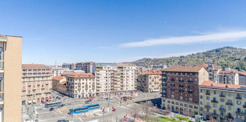 Una calle urbana con edificios y autobuses, frente a una colina verde.