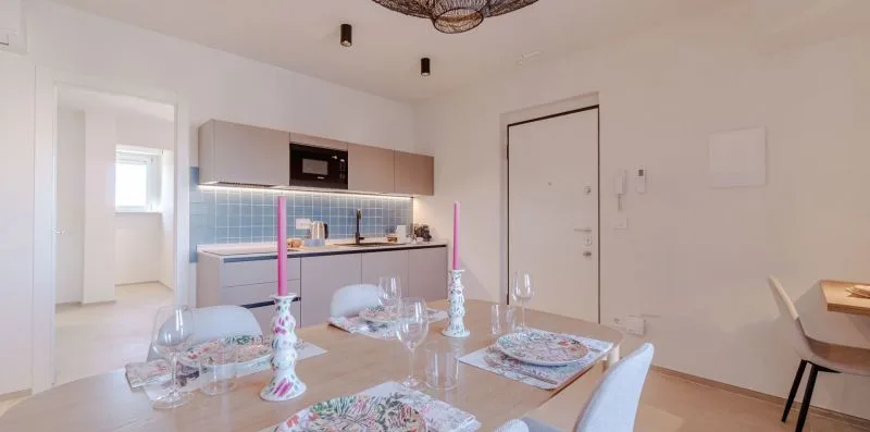Un comedor luminoso se abre a una cocina compacta con azulejos azules.