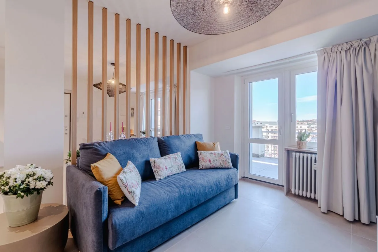 Una sala luminosa con asientos azules junto a ventanas altas y cortinas.