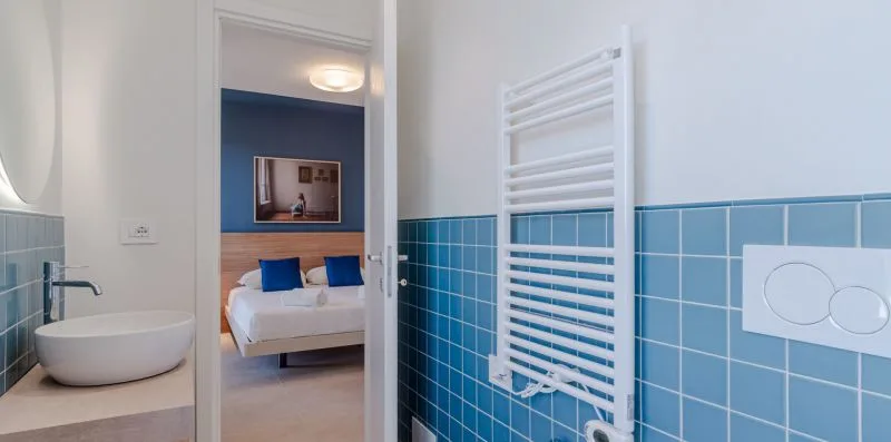 Un baño alicatado con un toallero calefactable y una puerta abierta que da a un dormitorio.