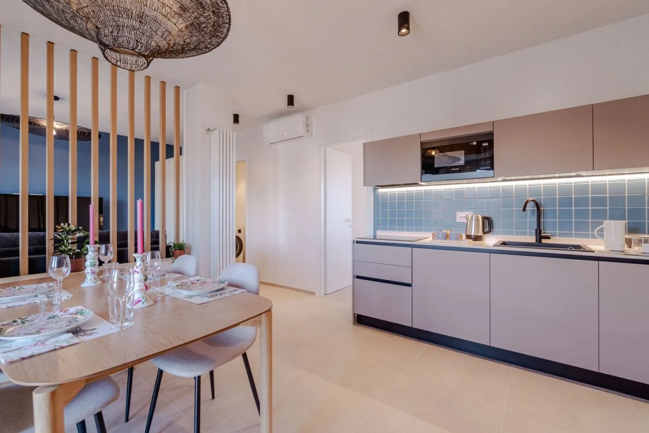 Un espacio abierto de comedor y cocina con una mesa junto a un salpicadero de azulejos azules.
