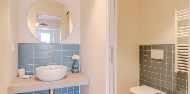 Un baño con lavabo y espejo redondo junto a una zona de ducha con azulejos.