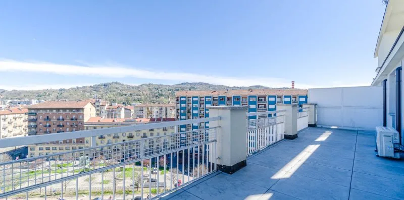 Una terraza en la azotea con barandillas metálicas da a edificios cercanos y colinas.