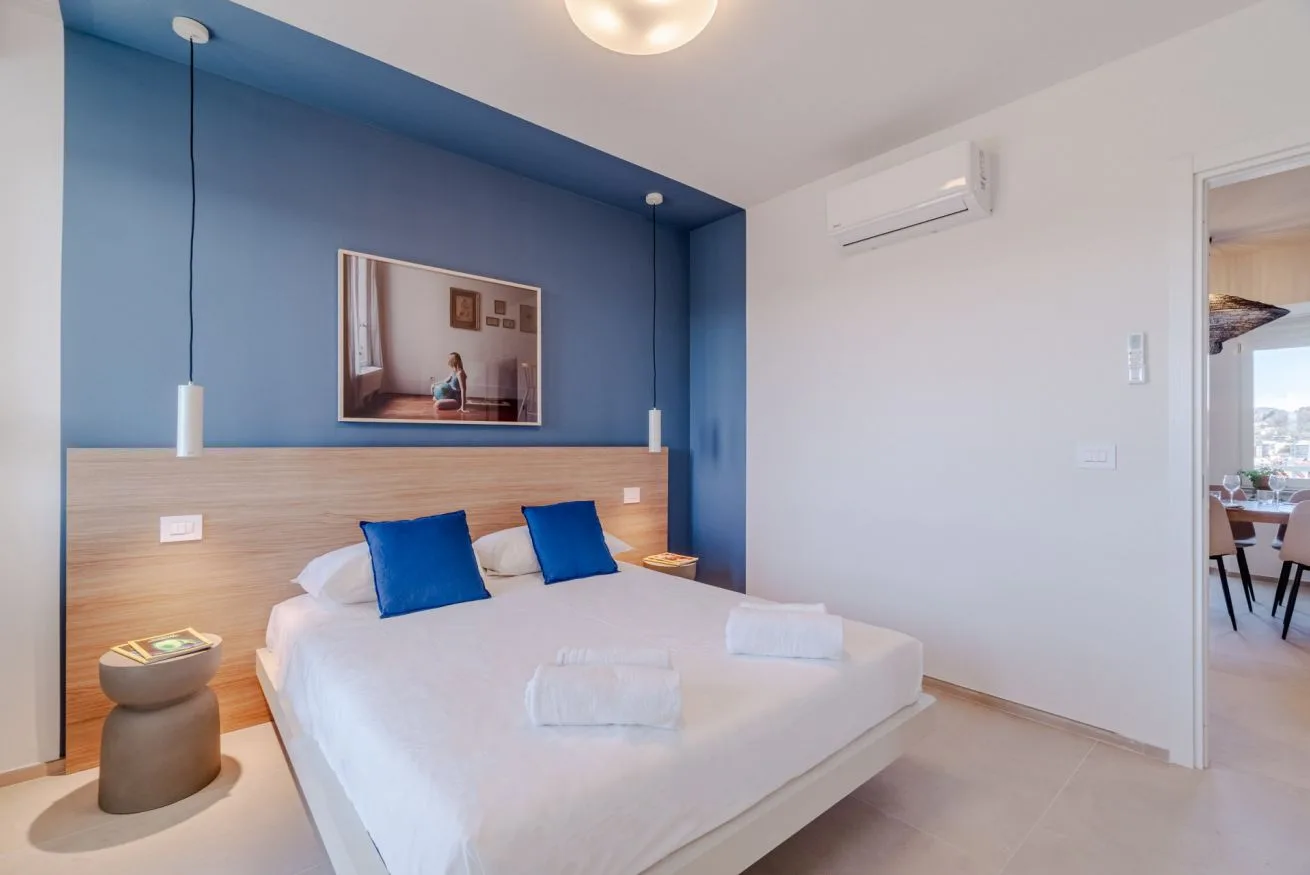 Dormitorio con una cama blanca, una pared azul y mesitas de noche.