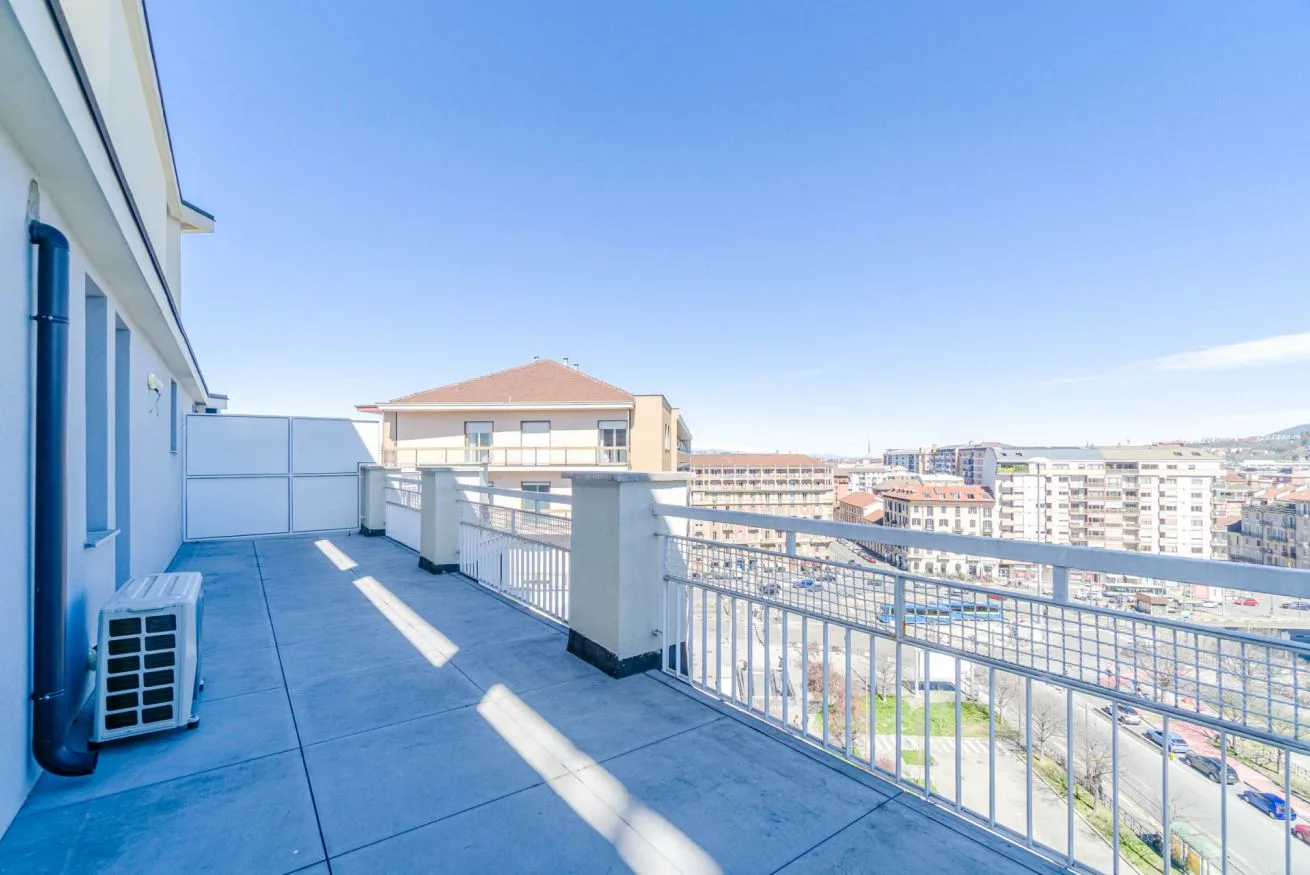 Una amplia terraza exterior tiene vistas a edificios cercanos bajo un cielo despejado.