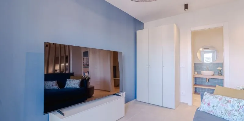 Un dormitorio con un televisor en una pared azul y armarios blancos.