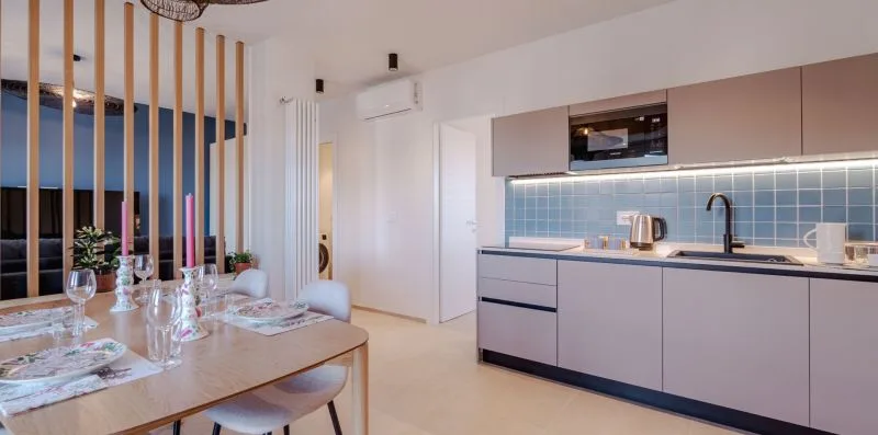 Comedor junto a una cocina moderna, con la mesa puesta y un salpicadero azul.