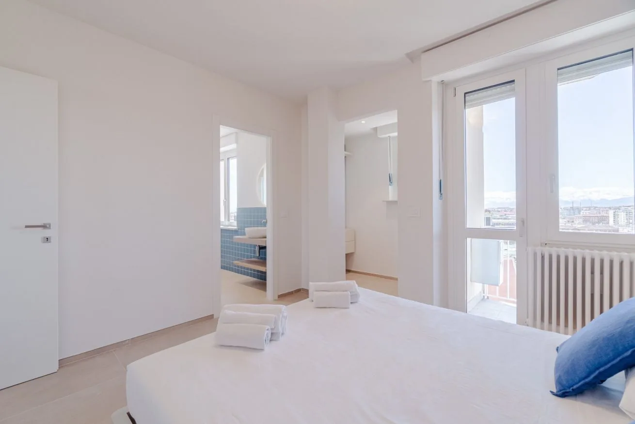 Un dormitorio luminoso con una cama junto a ventanas altas y un radiador.