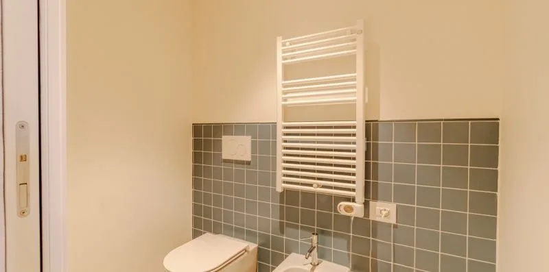 Una pared de baño alicatada con un radiador toallero blanco sobre el lavabo.