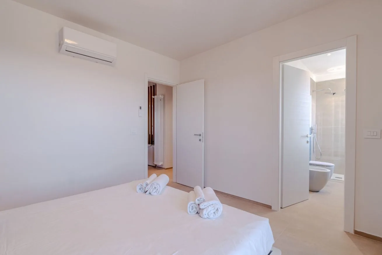 Un dormitorio luminoso con una cama bien hecha y una puerta abierta hacia un baño.