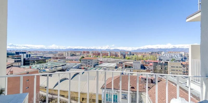 Un balcón ofrece vistas de tejados cercanos y del horizonte de la ciudad bajo un cielo despejado.