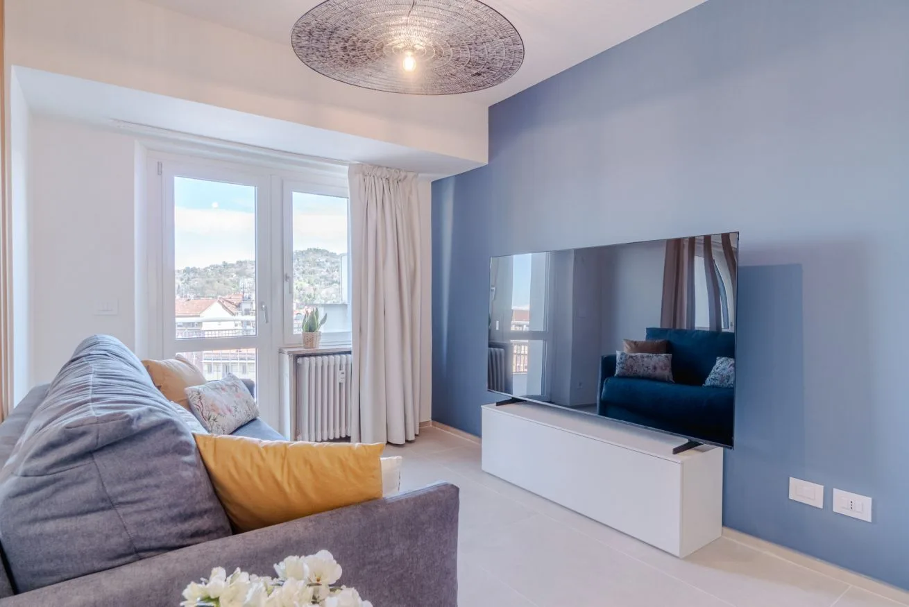Una sala de estar con asientos, un televisor y ventanas con vistas a tejados.