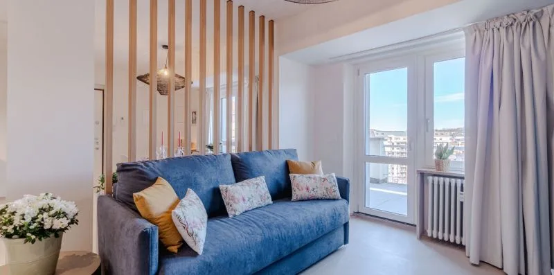 Una sala luminosa con un sofá azul junto a ventanas altas.