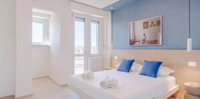 Un dormitorio luminoso con una cama, almohadas azules y una ventana grande.