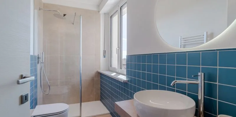 Un baño con ducha de cristal, lavabo de recipiente y paredes de azulejos azules.