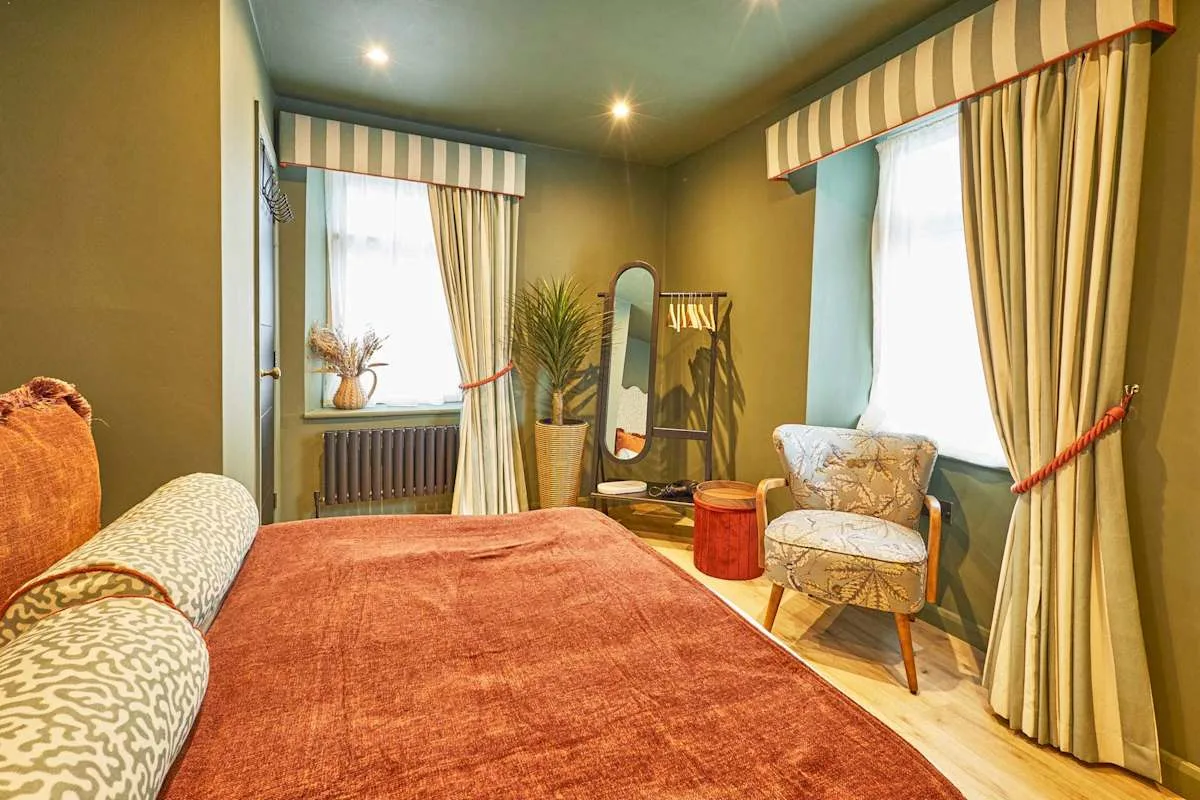 A bedroom with a bed, curtained windows, and a chair.