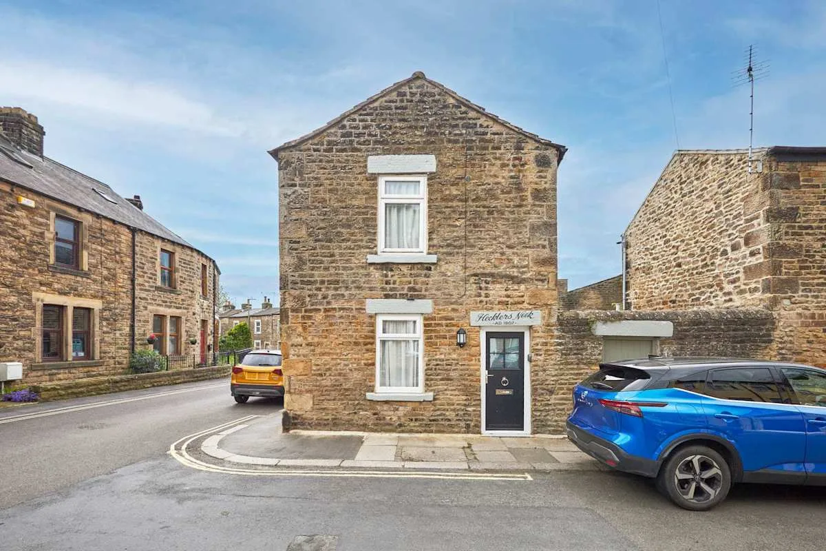 A stone house stands at a village street corner beneath a blue sky.