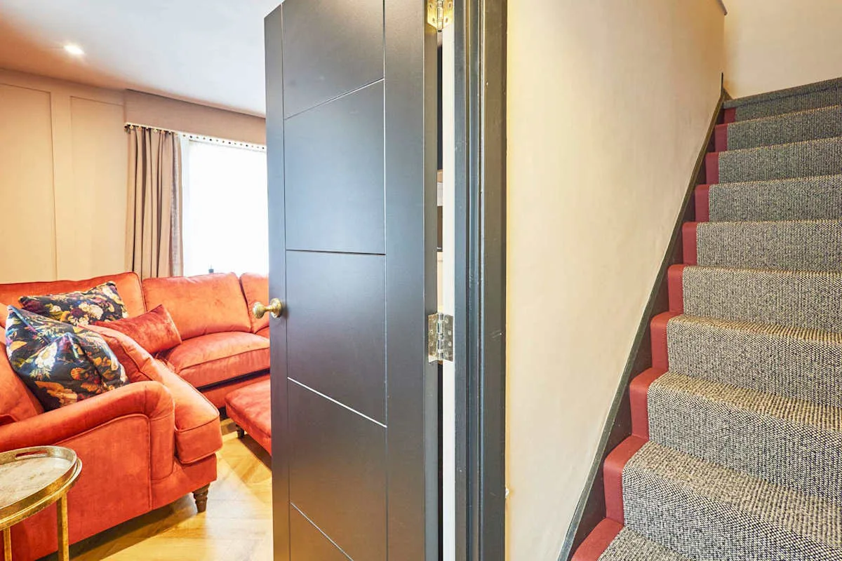 An interior doorway opens beside a carpeted staircase and a living area with seating.