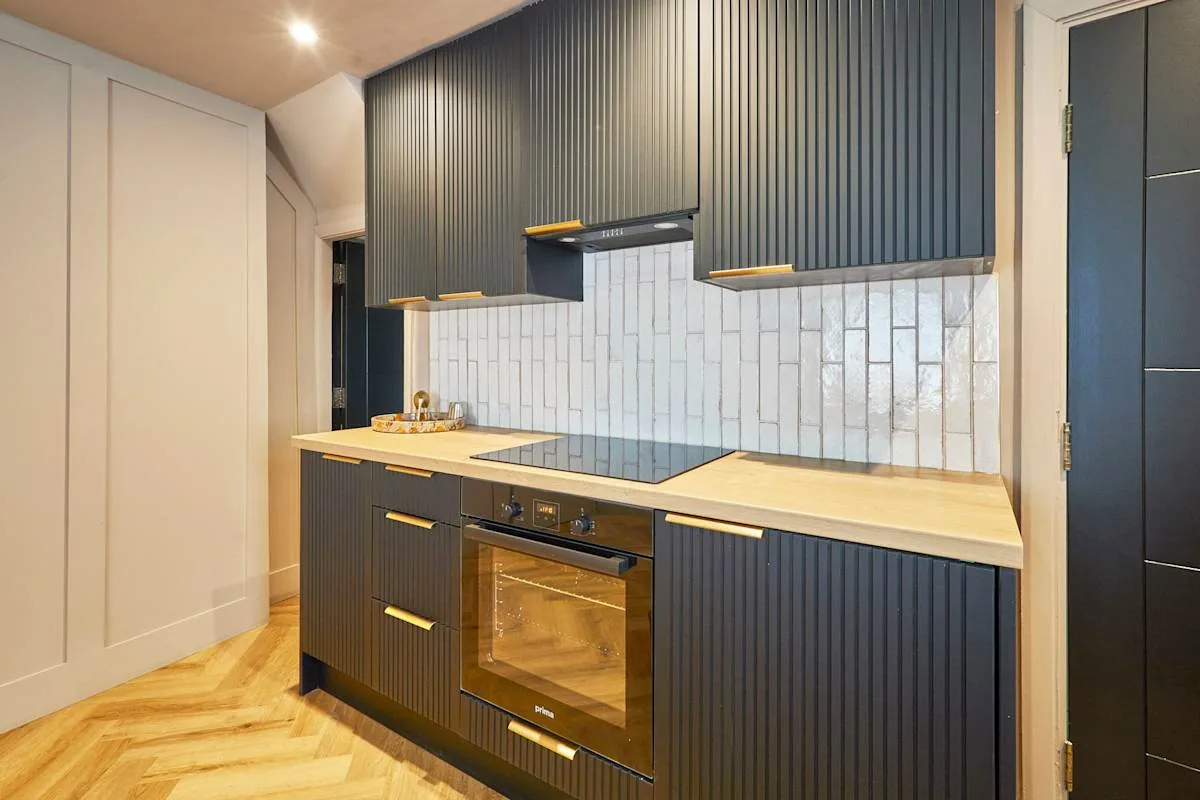 A modern kitchen with dark cabinets, a cooktop, and an oven.