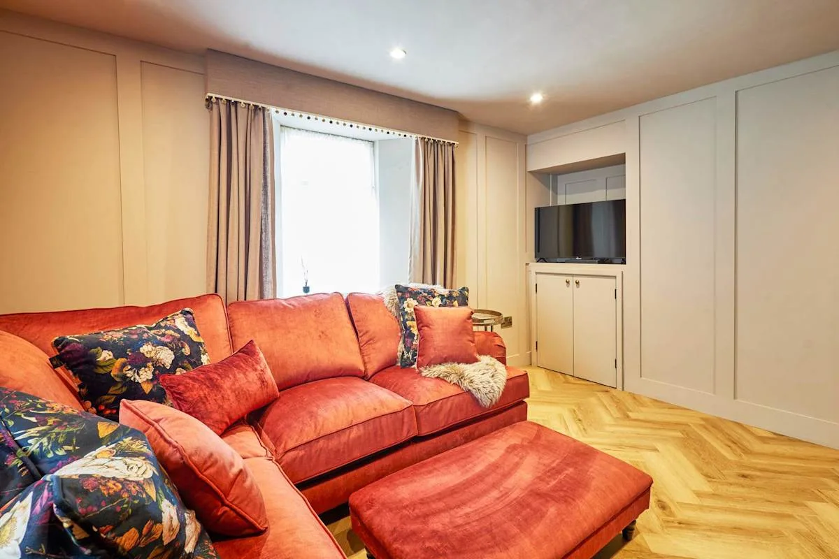 A living room with red seating, a matching footstool, and a television.